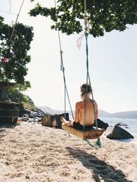 Man sitting on swing at beach against sky