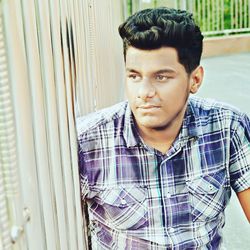 Thoughtful young man standing by metal fence