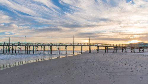 Pier on beach against sky during sunset