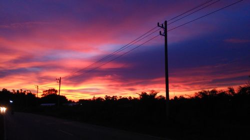 Silhouette electricity pylon against dramatic sky during sunset