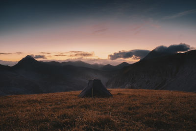 Tent on land with mountains in background against sky during sunrise