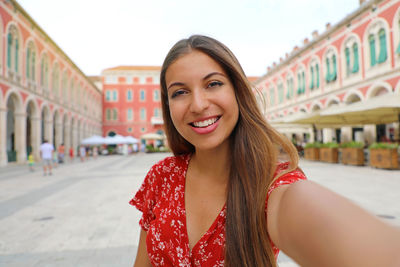 Portrait of smiling woman standing against buildings in town