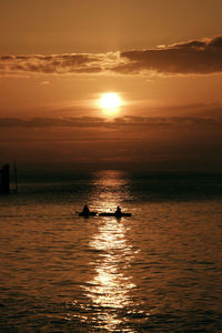 Silhouette swimming in sea against sky during sunset