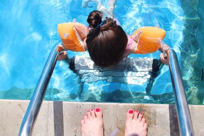 Low section of woman standing by girl on railing in swimming pool