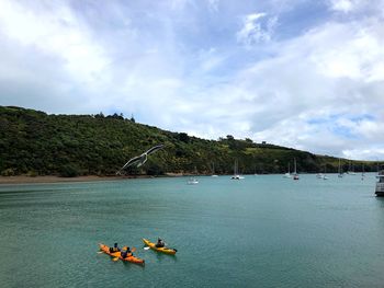 High angle view of people canoeing on sea against cloudy sky