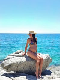 Pregnant woman sitting on rock by sea against sky