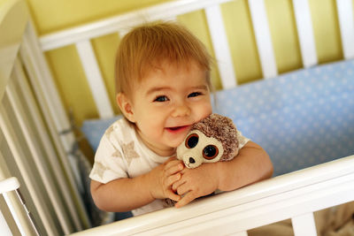Portrait of baby girl with toy standing in crib