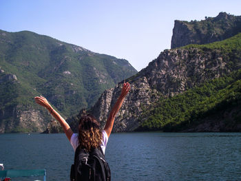 Rear view of woman with arms raised sanding by sea against sky