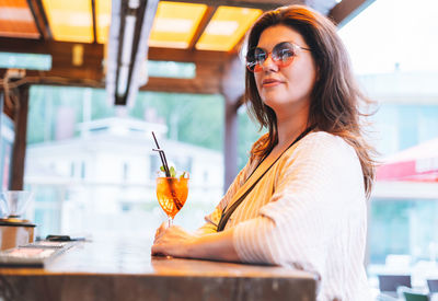 Stylish woman forty years plus size body positive in sunglasses drinking glass of cocktail 