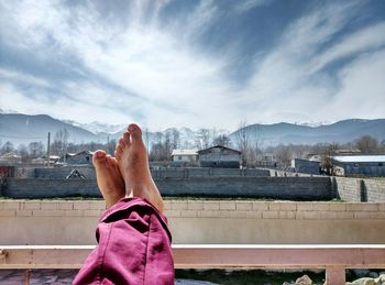 Low section of man with feet up of railing against sky