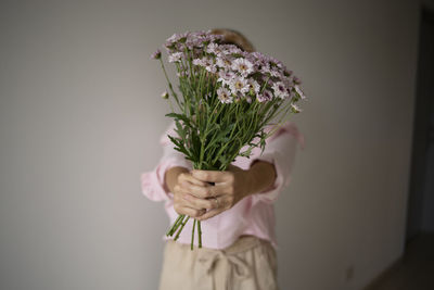 Woman holding bouquet while standing against wall