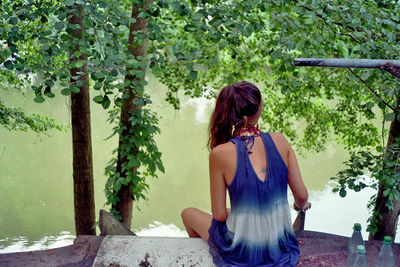 Rear view of young woman sitting by lake in forest