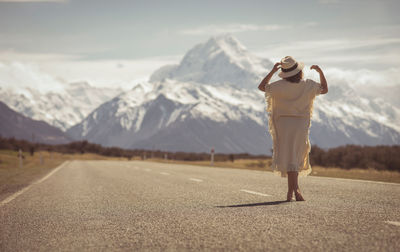 Rear view of mid adult woman standing on road against sky