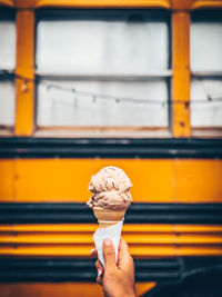 Human hand holding ice cream against bus