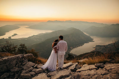 Rear view of couple standing on rock at beach against sky