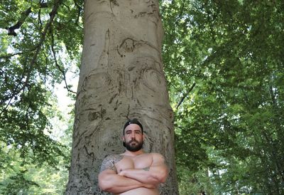 Portrait of young man against tree trunk in forest