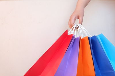 Cropped hand of person holding multi colored shopping bags against white background