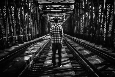 Rear view of man standing on railroad track at bridge