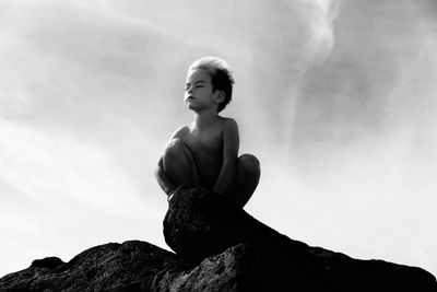 Low angle view of man sitting on rock against sky