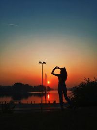 Silhouette man standing by lake against sky during sunset