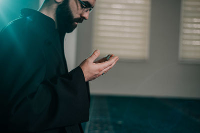 Side view of young man standing by window