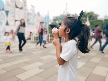 Side view of girl eating ice cream footpath in city