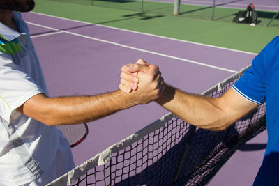 Friends shaking hands while standing on tennis court