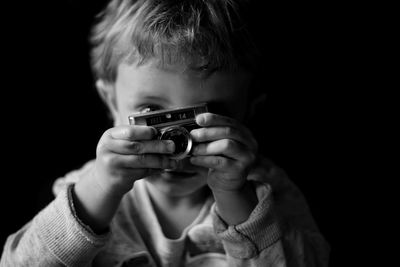 Midsection of child holding camera against black background