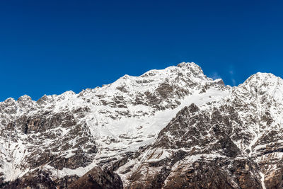 Low angle view of snowcapped mountains against clear blue sky