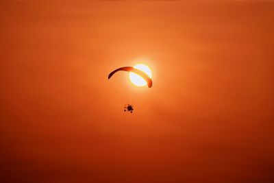 Low angle view of person paragliding against orange sky