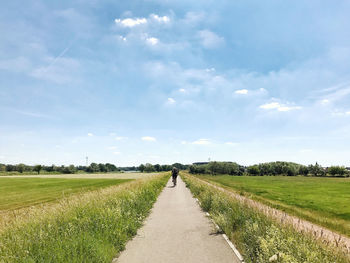 Empty road amidst field against sky