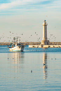 Fishing boat returning from fishing enters the port accompanied by seagulls, with lighthouse