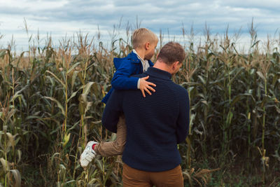 Family walking in corn field at autumn, dad and son posing among high plants