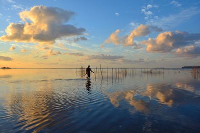 Silhouette person standing in sea against sky during sunset