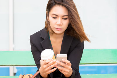 Young woman using smart phone while holding coffee cup