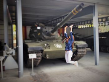Tilt-shift image of excited woman jumping against military tank