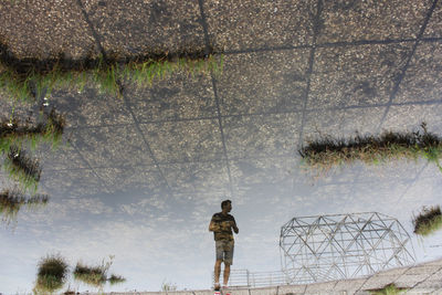Reflection of man in water puddle on footpath