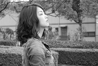 Close-up of thoughtful woman standing by hedge at park