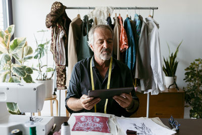 Mature tailor using digital tablet while working at studio