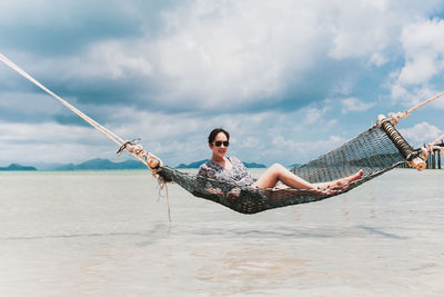Woman relaxing in hammock on a beach against blue sky