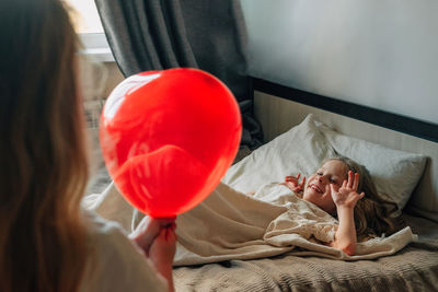 Children play at home on the bed with a red balloon