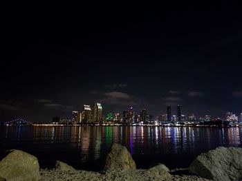 Illuminated buildings by sea against sky at night