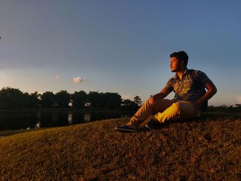 Man sitting on land against sky during sunset