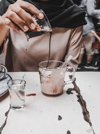 Midsection of woman pouring black coffee in cup on table