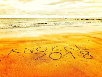 Text on sand at beach against sky