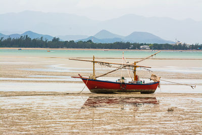 Fishing boat moored on beach against sky