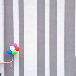 Cropped image of hand holding balloons against striped wall