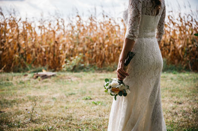 Midsection of bride holding flowers on field