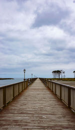 Pier on footbridge over sea against sky