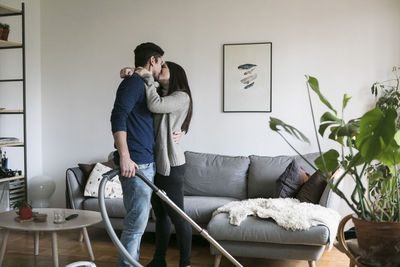 Couple kissing while cleaning living room at home